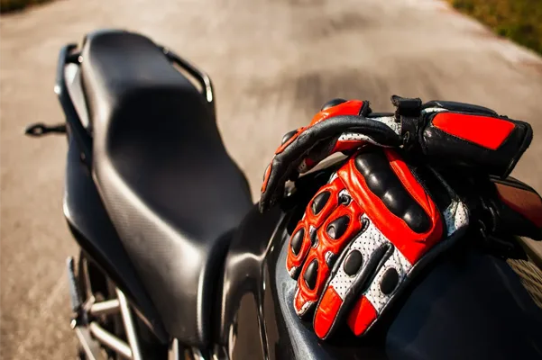 Close-up of a red and black motorcycle glove on a handlebar with a blurred road background