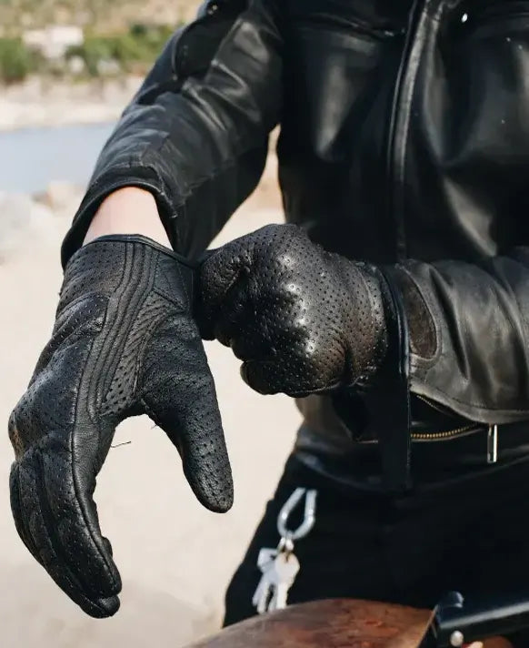 Person wearing black leather gloves and a jacket outdoors.