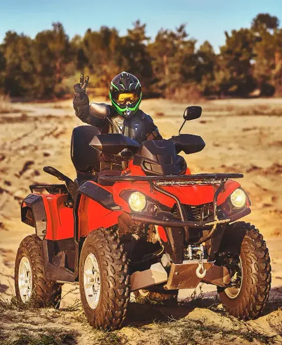 Person riding a red ATV in an open field with trees in the background
