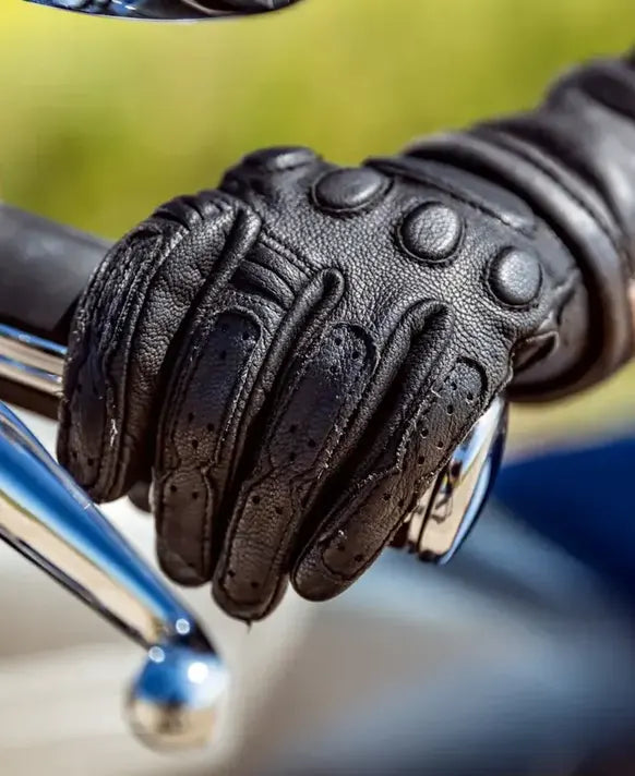 Black leather glove on a motorcycle handlebar with a blurred background