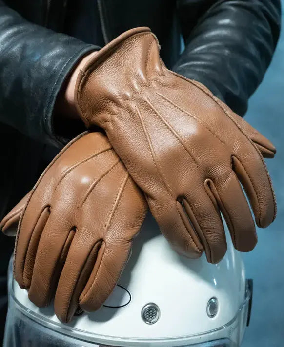 Brown leather gloves held over a white helmet against a blurred background